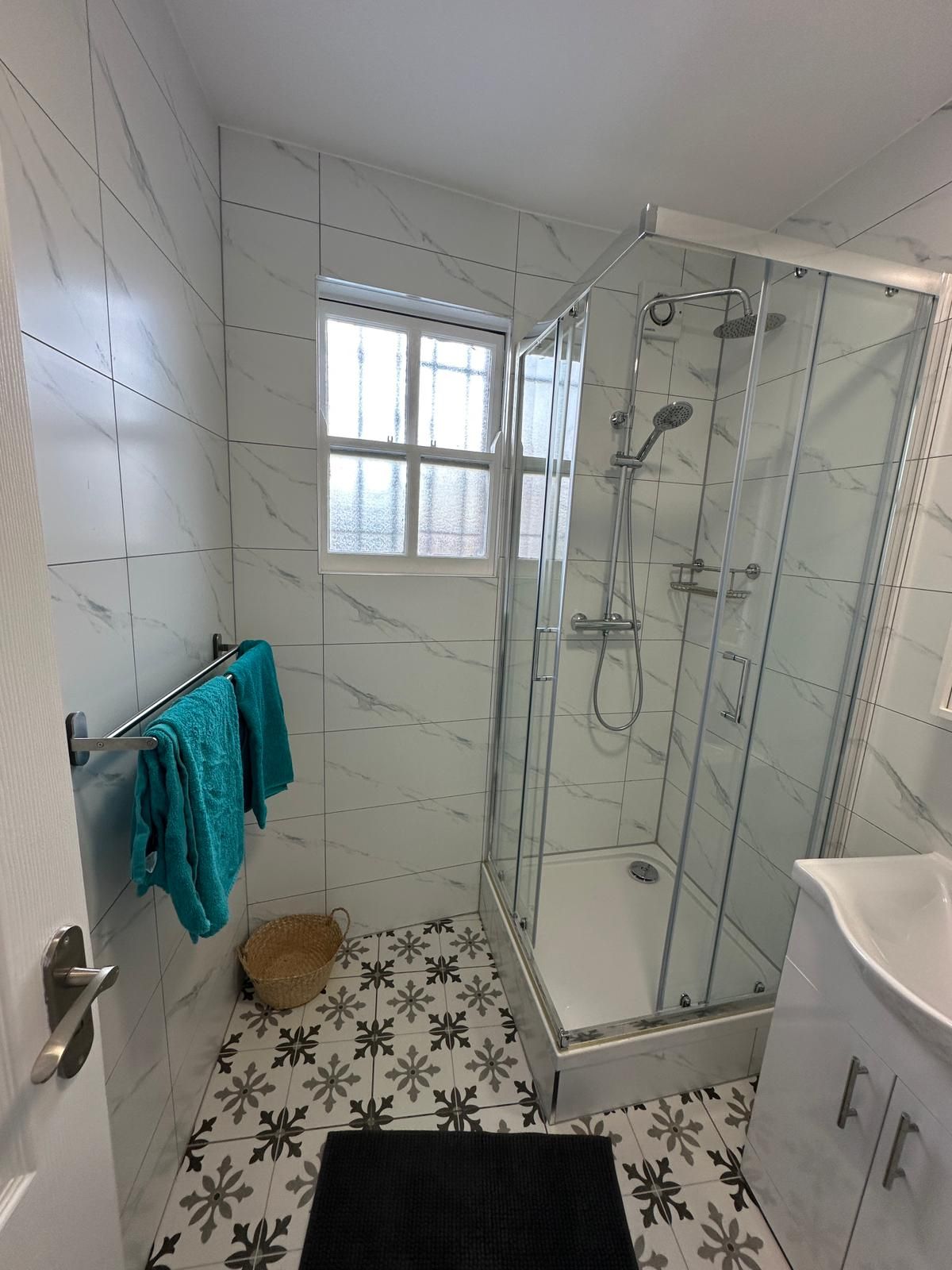 A bathroom with a glass-enclosed shower, a window, and a towel rack with towels.