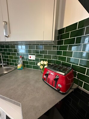 A kitchen with a red toaster, a sink, and green tiled backsplash. - Private Room with Private Kitchen & Bathroom (London)