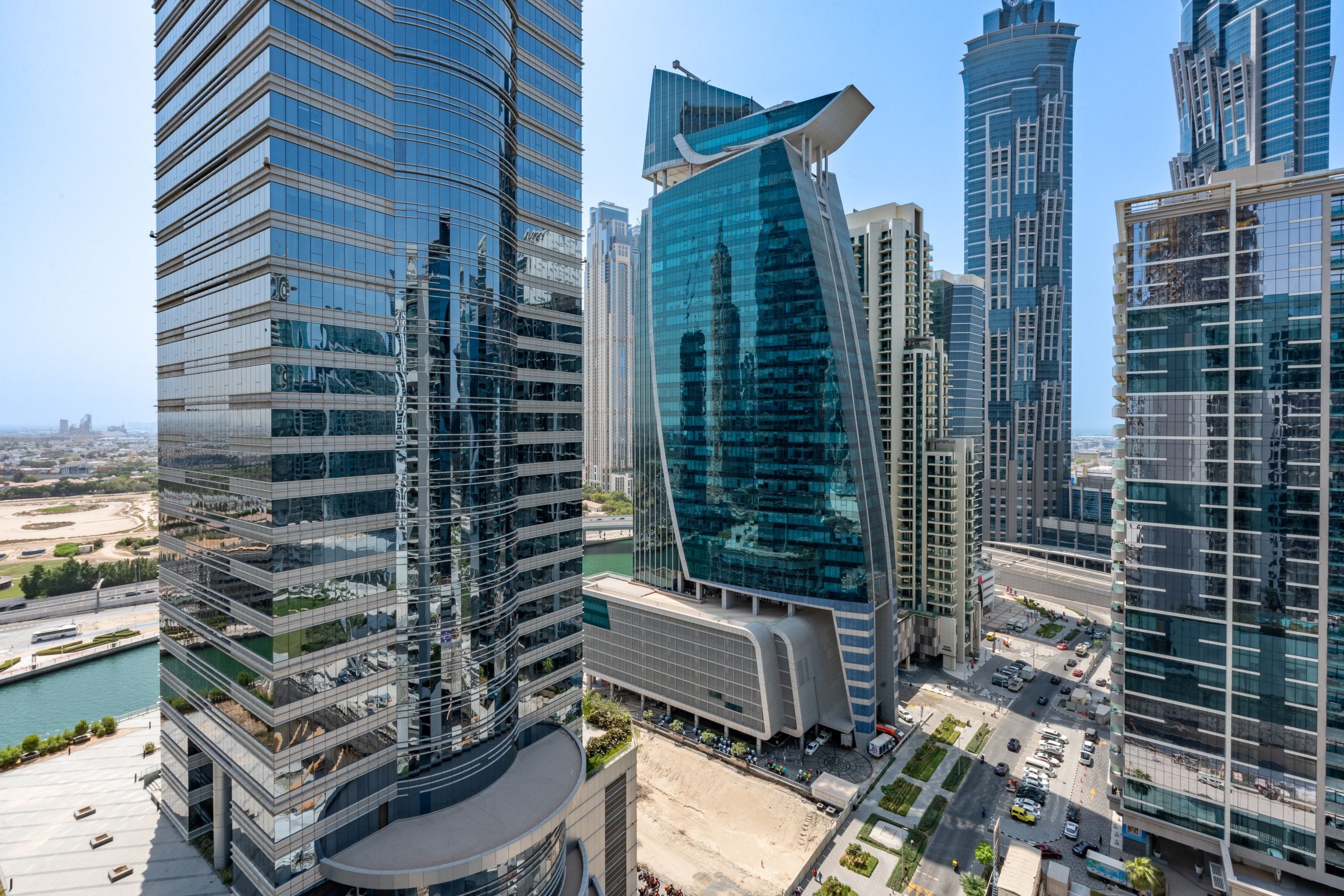 A modern high-rise building with a curved glass facade, surrounded by other tall buildings.