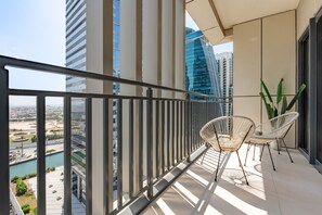 A balcony with a view of a cityscape, two white wicker chairs, and a potted plant. - Premium 1BR with Canal and City Views, Near Marine Transport (Dubai)