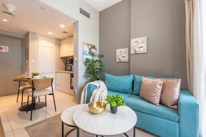 A modern living room with a teal sofa, a coffee table, and a dining area with a small table and chairs. - Premium 1BR with Canal and City Views, Near Marine Transport (Dubai)