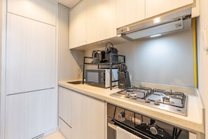 A compact kitchen with a microwave, toaster, and gas stove. - Premium 1BR with Canal and City Views, Near Marine Transport (Dubai)