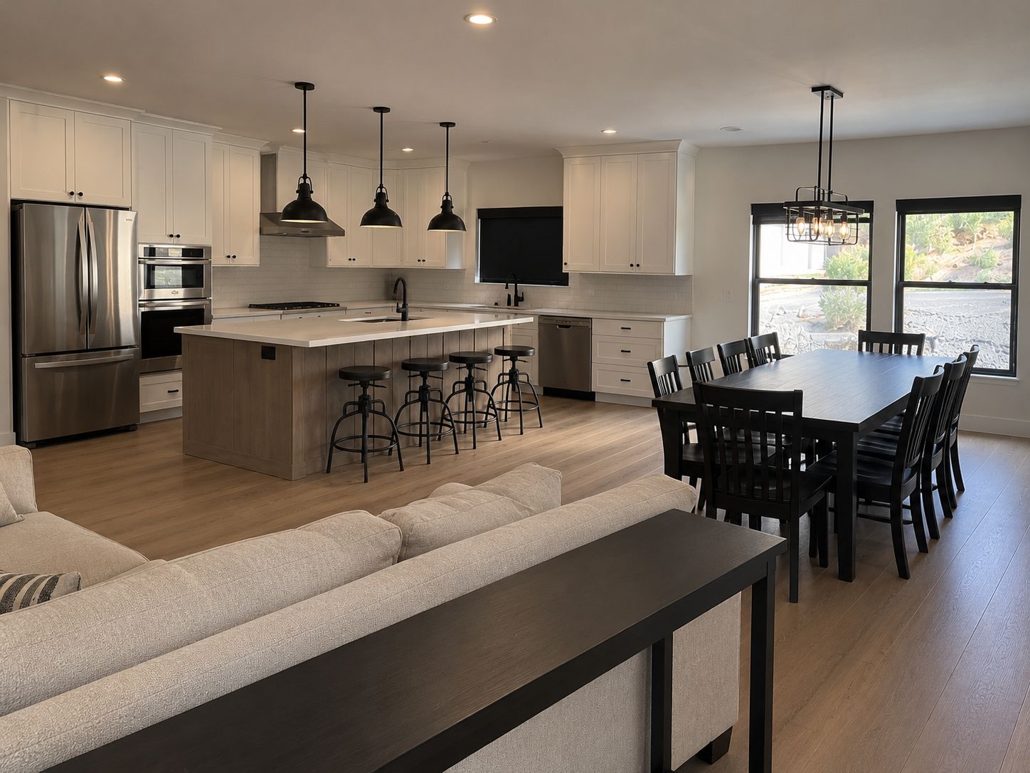 A modern kitchen with a central island, bar stools, a dining table with chairs, and a large window providing a view.