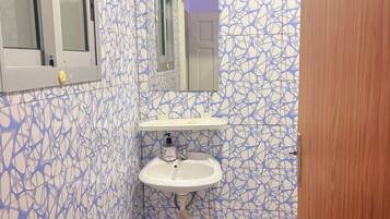 A bathroom with a sink, mirror, window, and a trash bin.