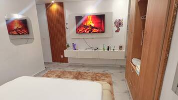 A modern bedroom with a large bed, a TV mounted on the wall, a wardrobe, and a small side table.