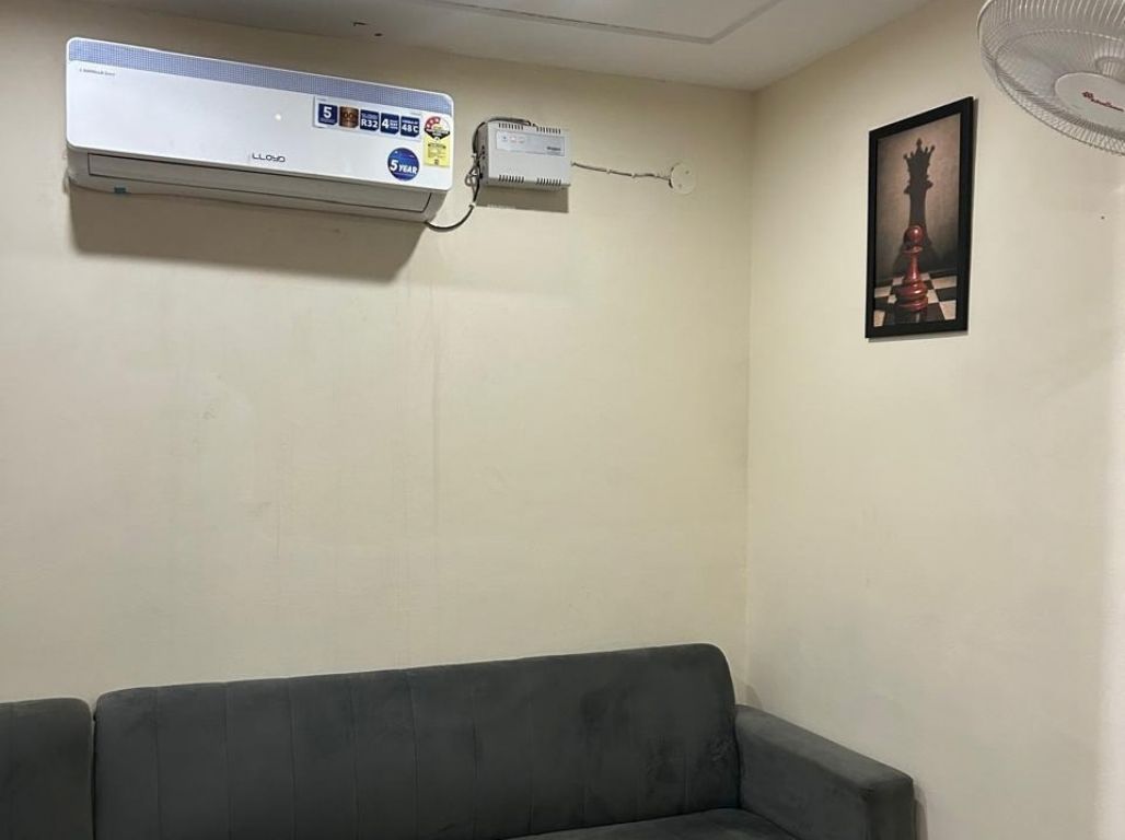 A room with a grey sofa, an air conditioning unit, a wall-mounted fan, and a chessboard artwork.