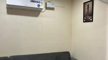 A room with a grey sofa, an air conditioning unit, a wall-mounted fan, and a chessboard artwork.