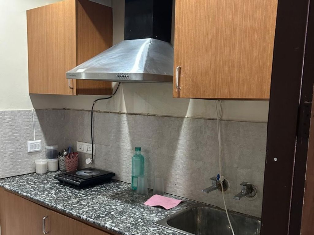 A kitchen with a stainless steel range hood, a granite countertop, a sink, and wooden cabinets.