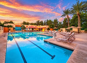 Una piscina amb gandules i ombrelles, envoltada de palmeres i un edifici amb teulada vermella.
