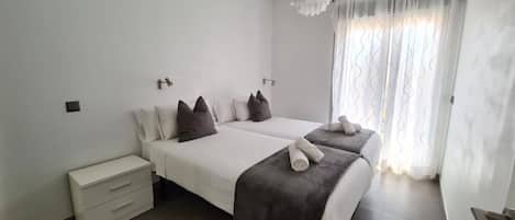 Habitación de hotel con dos camas, una mesita de noche y una ventana con cortinas.
