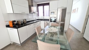 A modern kitchen with a glass dining table, white cabinets, and stainless steel appliances. - La Cruz 8 Apartament SilHouse (Nerja)
