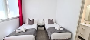 A hotel room with two single beds, a nightstand, a small table, and a window with a red curtain. - La Cruz 8 Apartament SilHouse (Nerja)