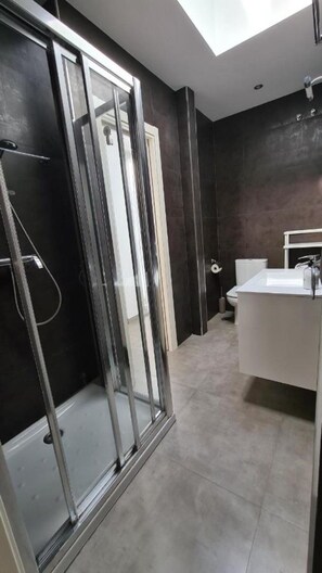 A modern bathroom with a glass shower enclosure, a white sink, and dark tiled walls. - La Cruz 8 Apartament SilHouse (Nerja)