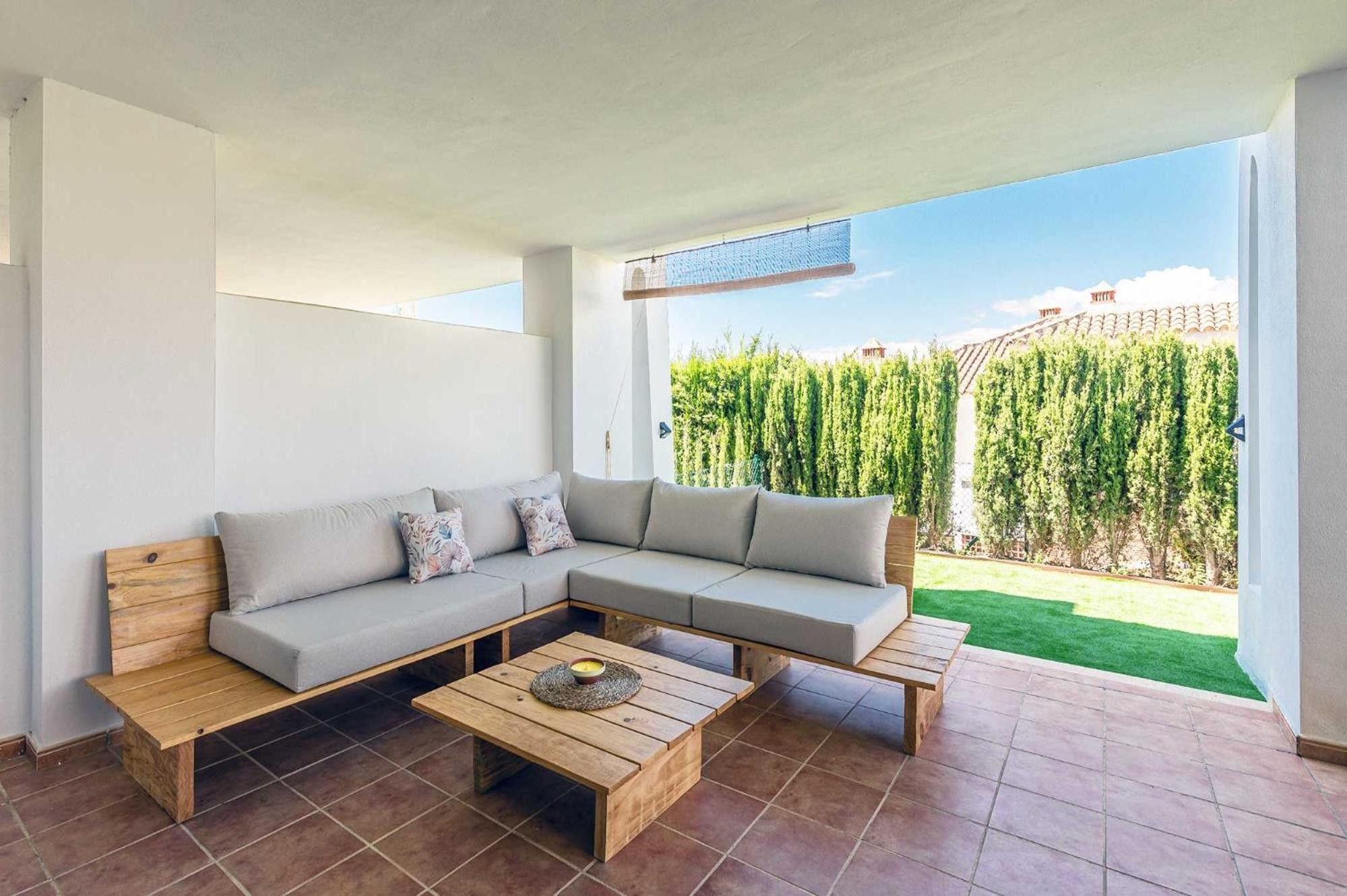 Un salon moderne avec un canapé d’angle, une table basse en bois et une vue sur un jardin bien entretenu.