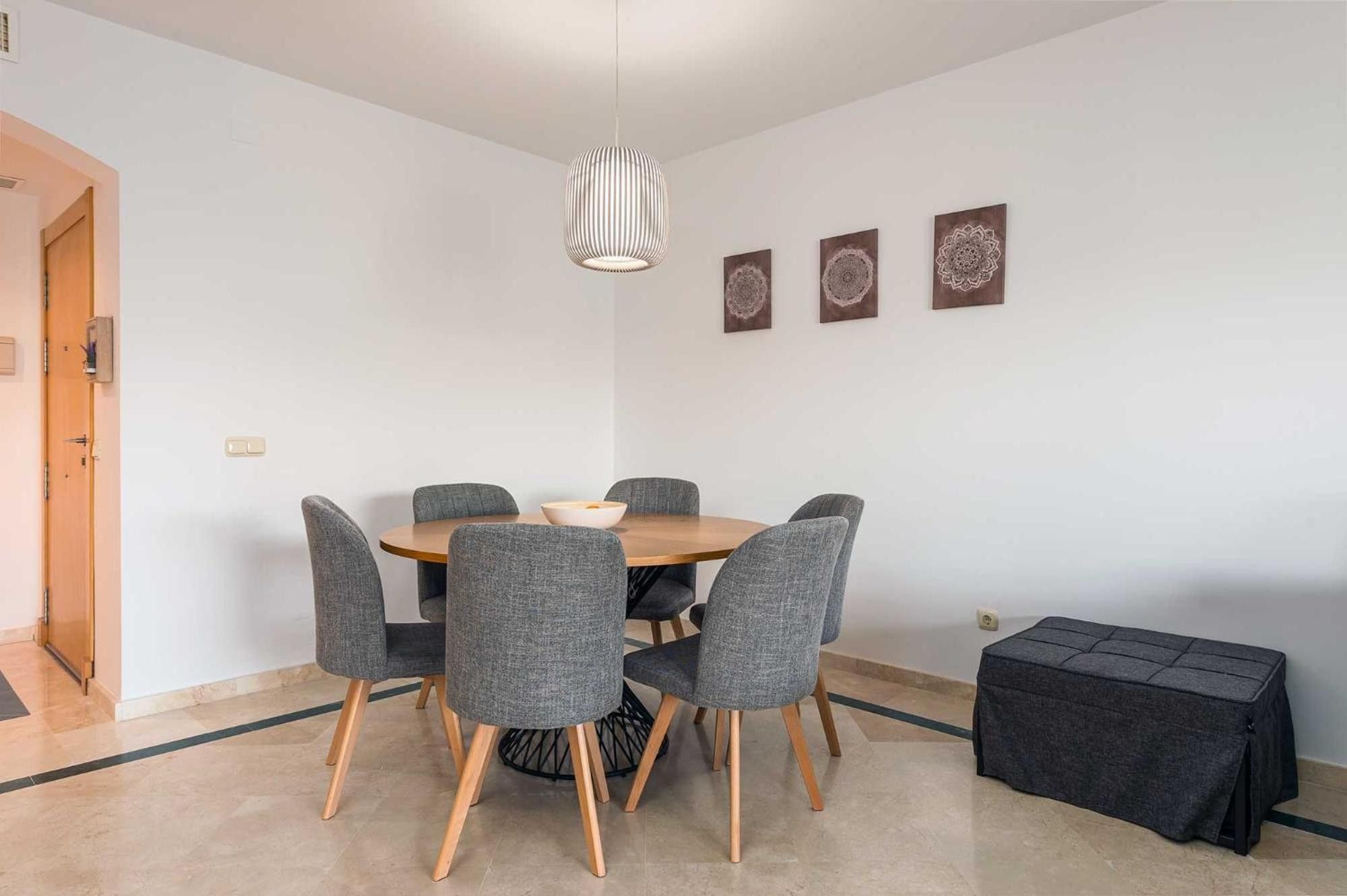 Un'area pranzo con un tavolo rotondo, sei sedie grigie imbottite, un lampadario e tre pannelli decorativi a parete.