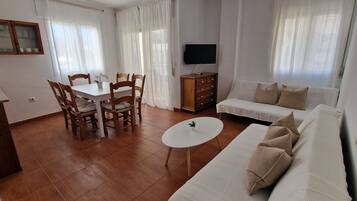 A living room with a dining area, a sofa, a TV, and a small table.