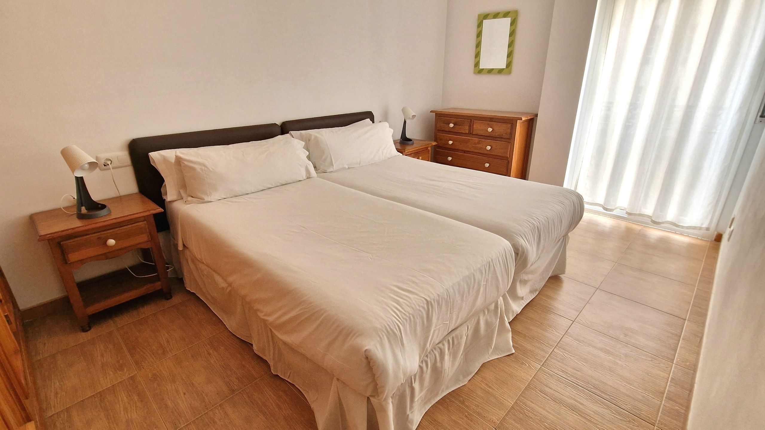 Una cama doble con cabecera de madera, una mesita de noche con lámpara y un aparador.