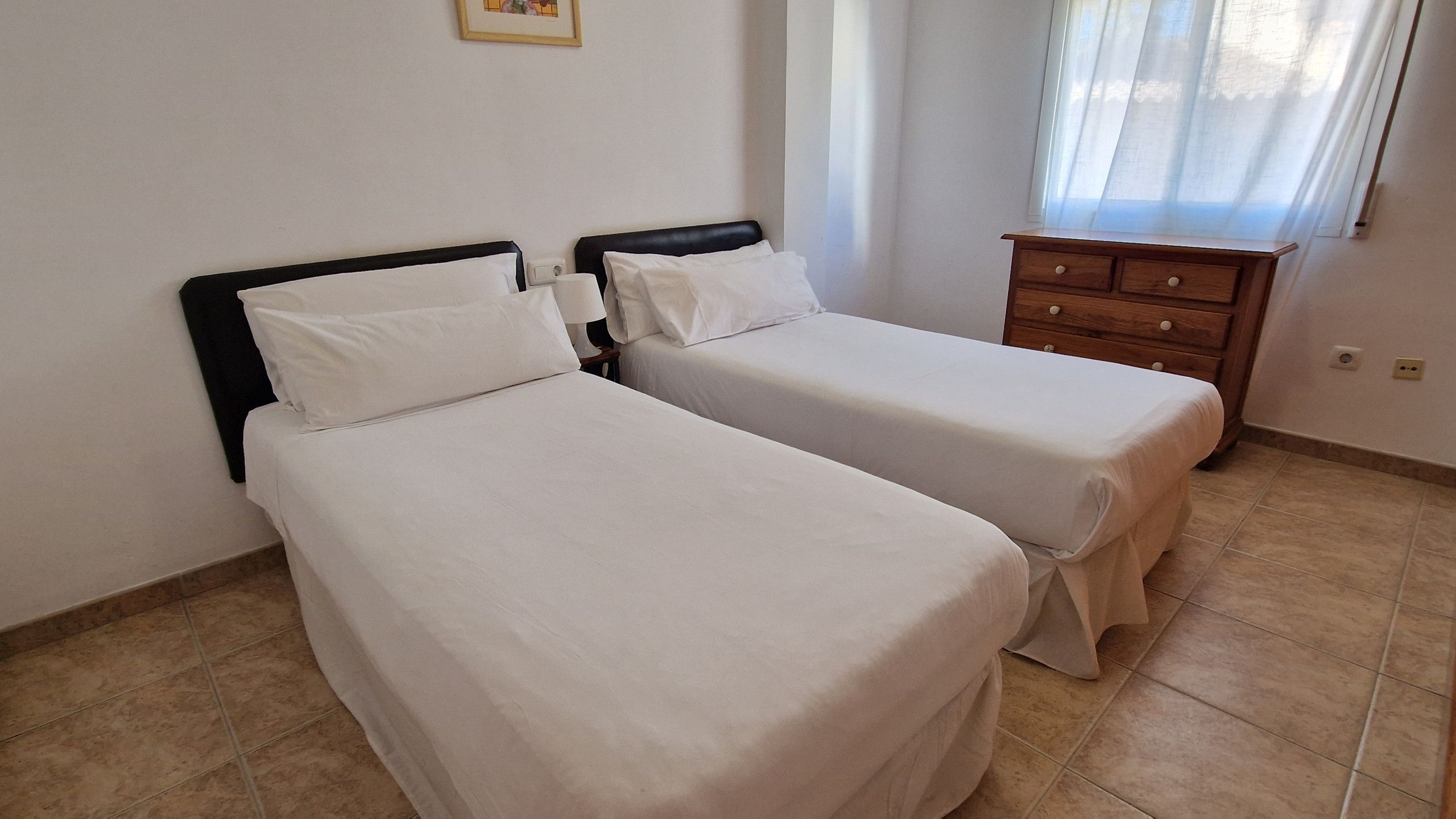 Una habitación con dos camas individuales, un aparador de madera y una ventana con cortinas.