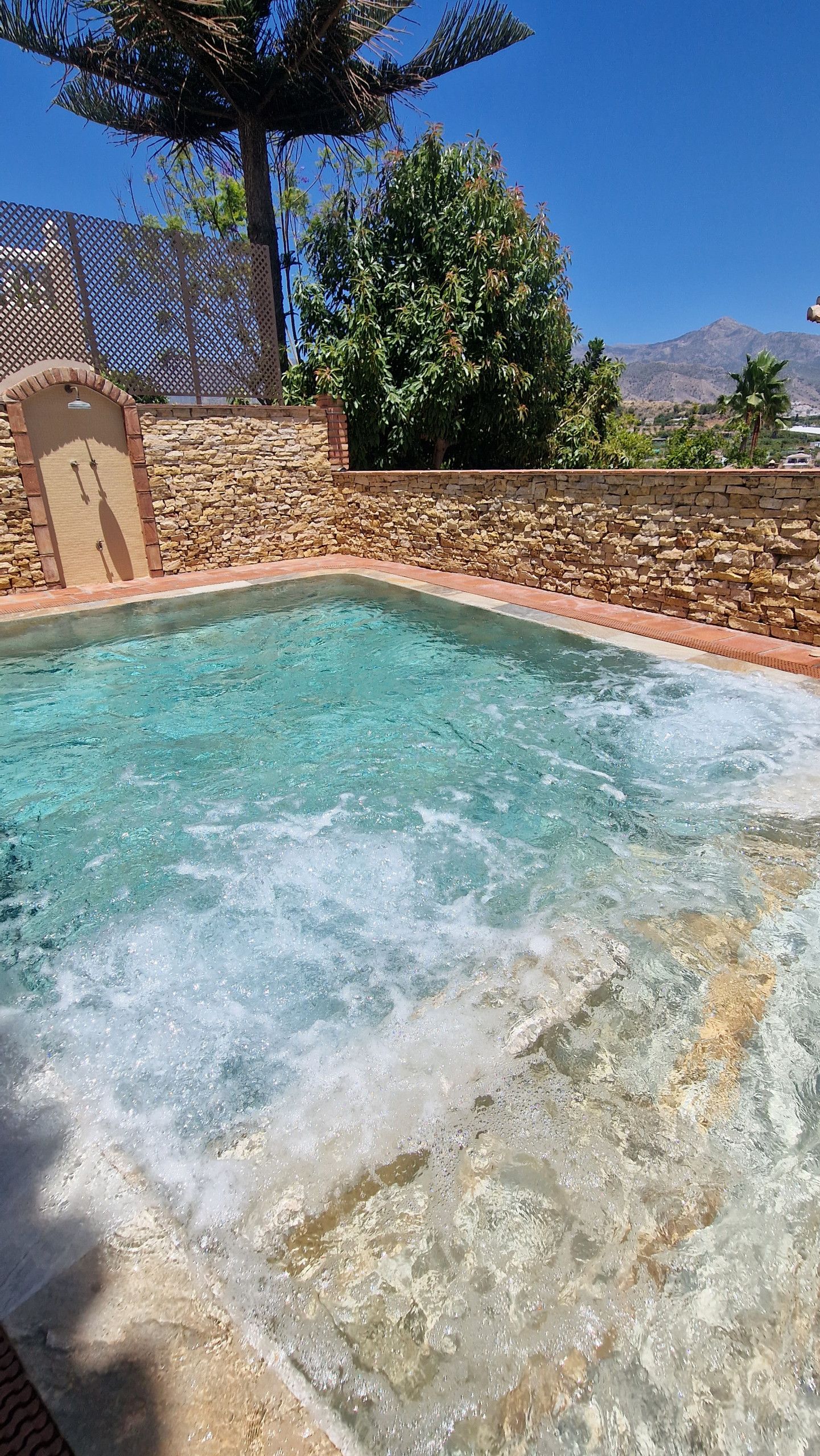 Ein Schwimmbecken mit einer Steinmauer und einer Holzpergola.