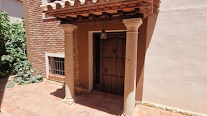 Una entrada de edificio con puerta de madera, pared de ladrillo y patio con baldosas.