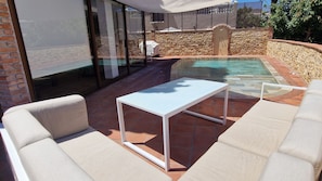 Un patio con piscina, mobiliario exterior y una pared de piedra.