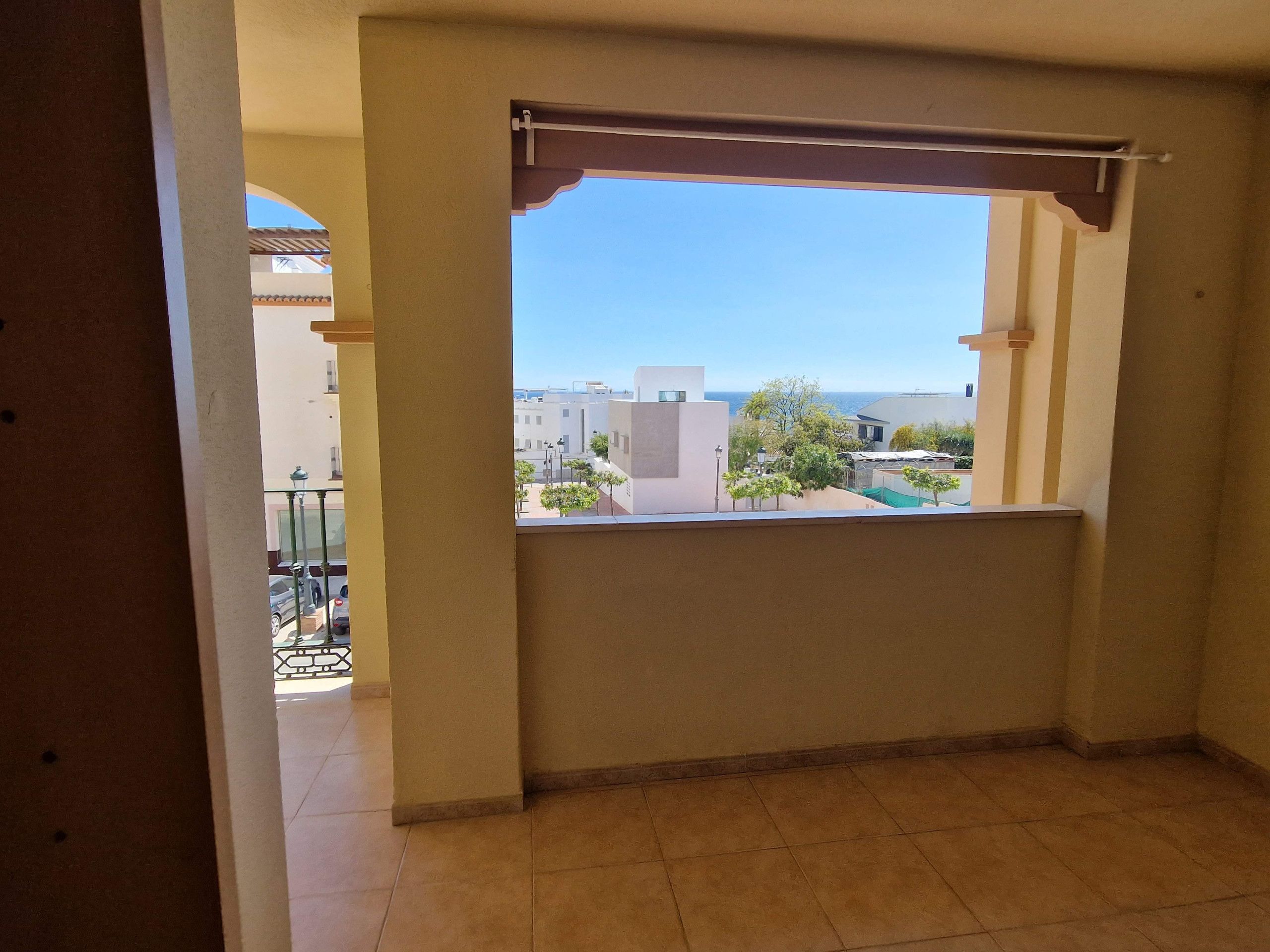 Una habitación con ventana que da a una zona residencial, suelo de baldosas y un balcón con barandilla.