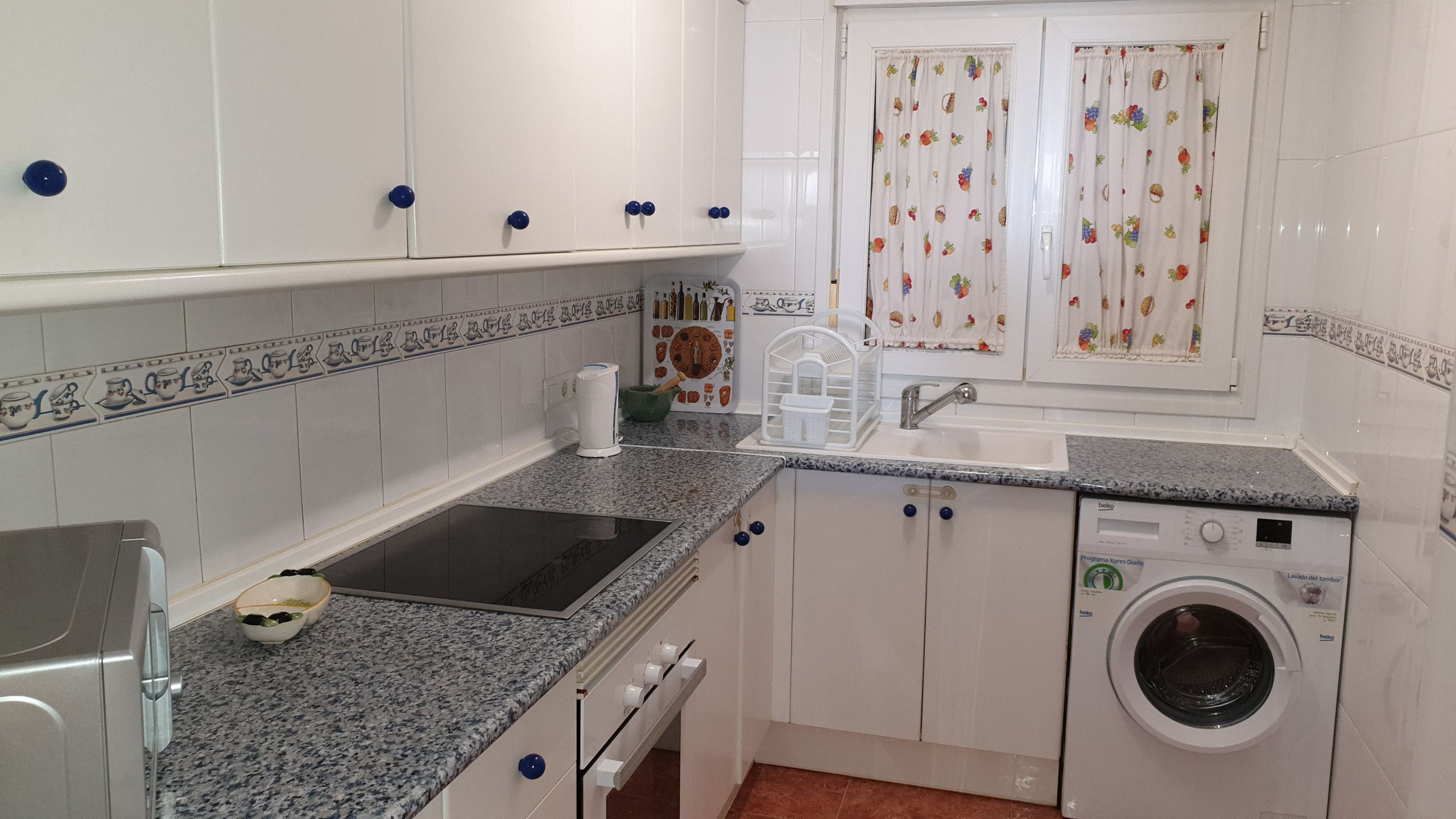 Una cocina funcional con armarios blancos, horno integrado, lavabo y lavadora.