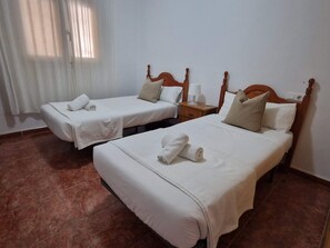 Una habitación de hotel con dos camas individuales, cada una con cabecero de madera, ropa de cama blanca y una toalla enrollada.