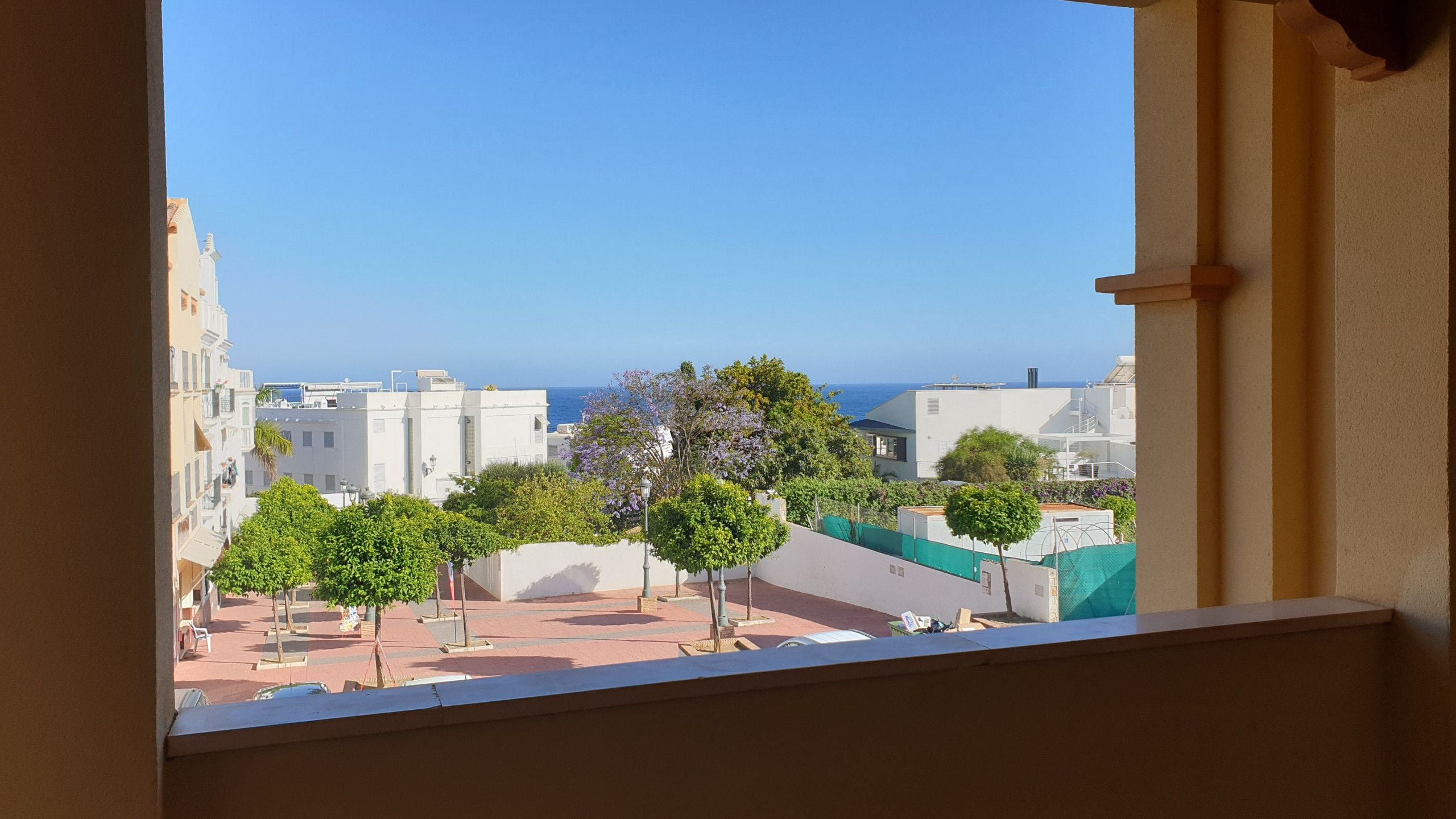 Vista desde una ventana sobre una zona costera con edificios y árboles.