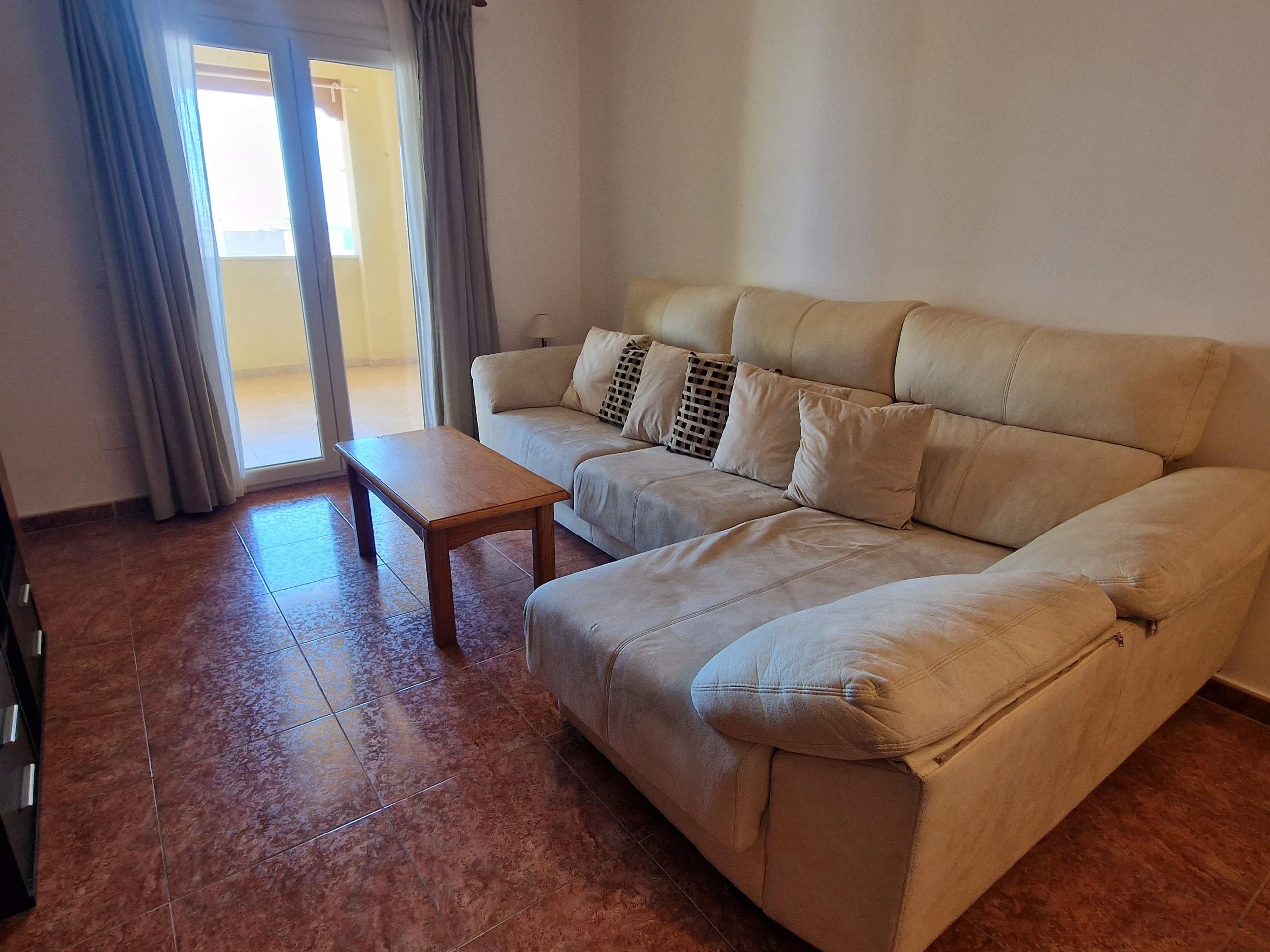 Una sala de estar con un sofá color beige, una mesa de centro de madera y un ventanal corredizo.