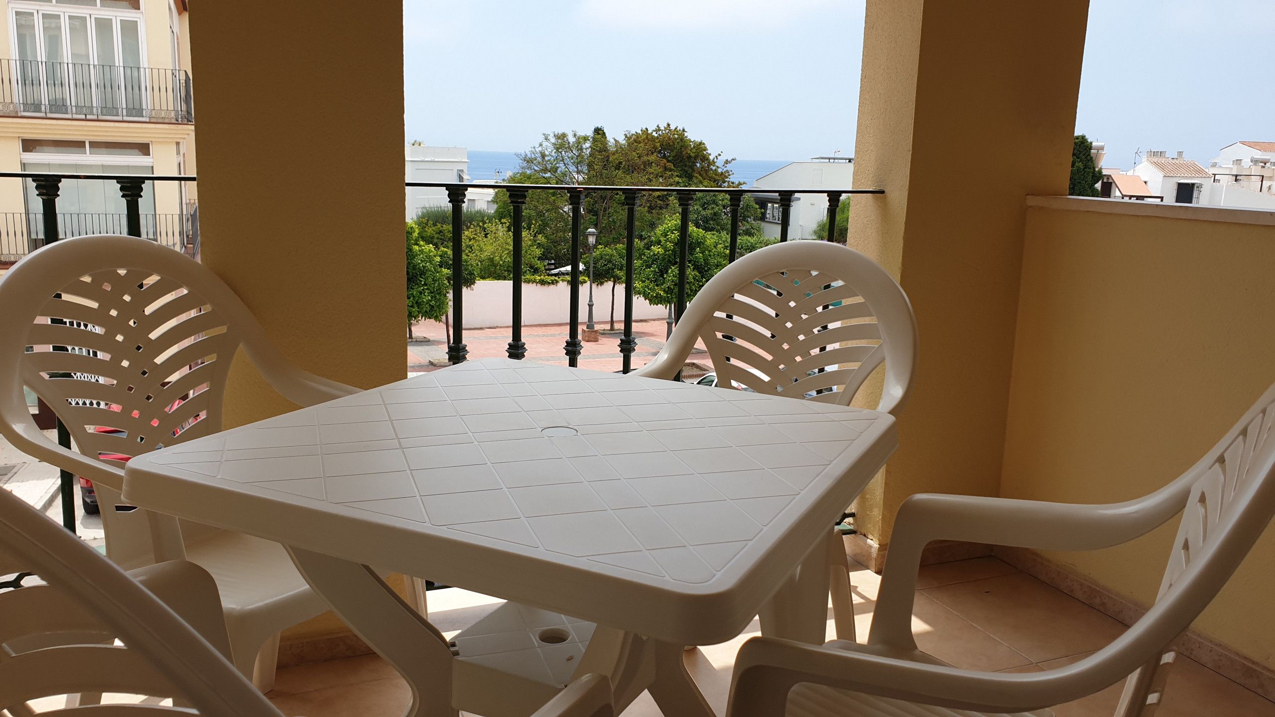 Un balcón con una mesa y sillas blancas, vista al mar y barandilla.