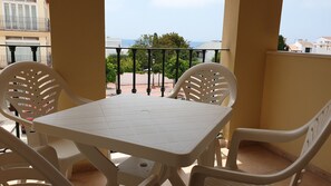 Un balcón con una mesa y sillas blancas, vista al mar y barandilla.