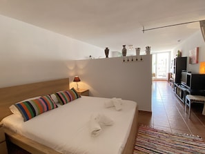 Ein Hotelzimmer mit Bett, Nachttisch, Lampe, Fernseher und Blick ins Freie.