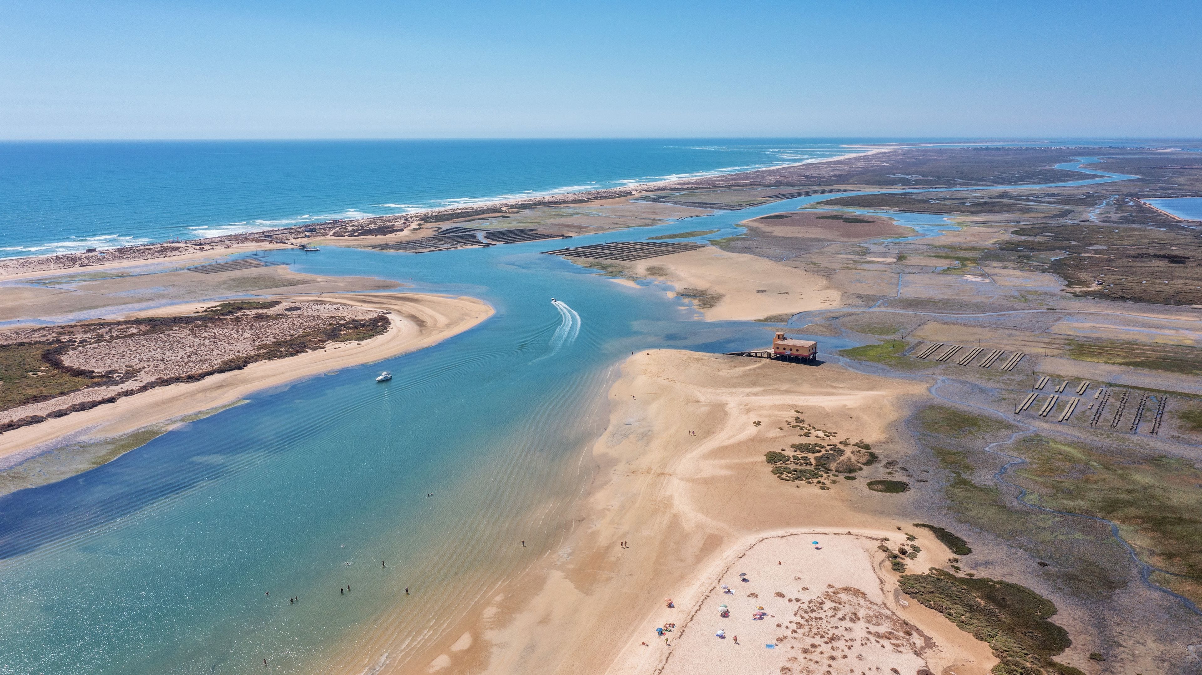 Vista aérea de uma área costeira com praia, um barco e uma estrutura sobre pilares.