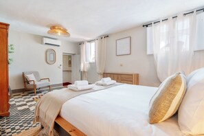 A bedroom with a bed, a chair, an air conditioning unit, and a window with curtains. - Privilege St George House 5 Bedrooms & Hot Tub in the heart of Fuseta (Fuseta)