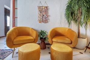 A room with two armchairs and ottomans, a hanging wall decoration, a potted plant, and a large potted tree. - Privilege St George House 5 Bedrooms & Hot Tub in the heart of Fuseta (Fuseta)