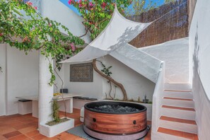 A spa area with a hot tub, a white wall with a decorative tile, and a tree with pink flowers. - Privilege St George House 5 Bedrooms & Hot Tub in the heart of Fuseta (Fuseta)