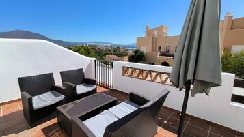 A terrace with wicker furniture, a table, and an umbrella.