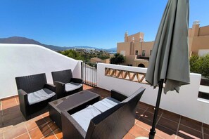Una terraza con muebles de mimbre, una mesa y una sombrilla.