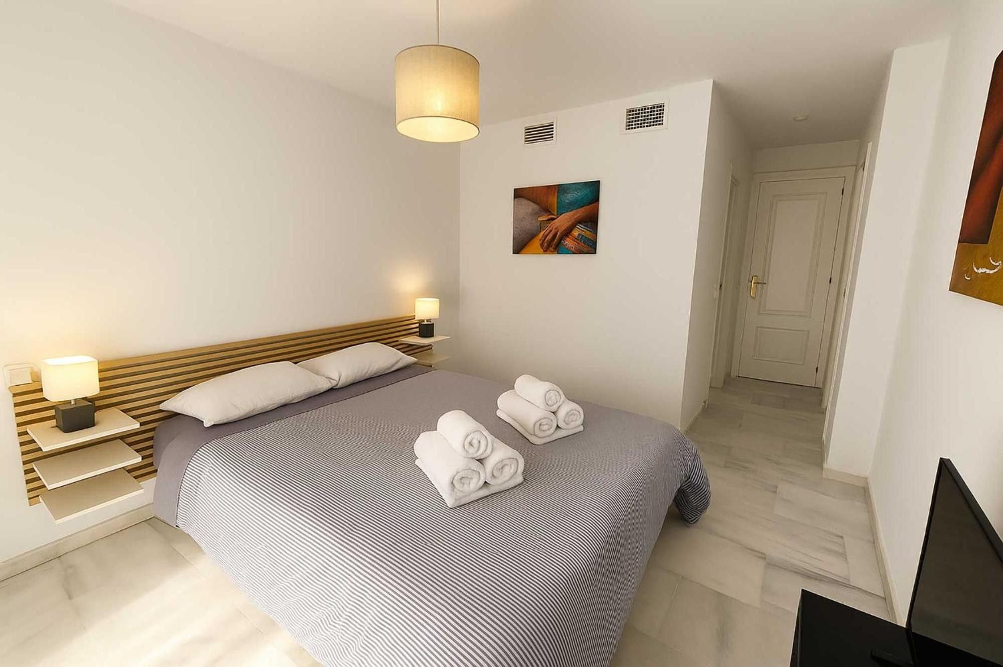 Une chambre d’hôtel avec un lit, des lampes de chevet, un tableau et une porte.