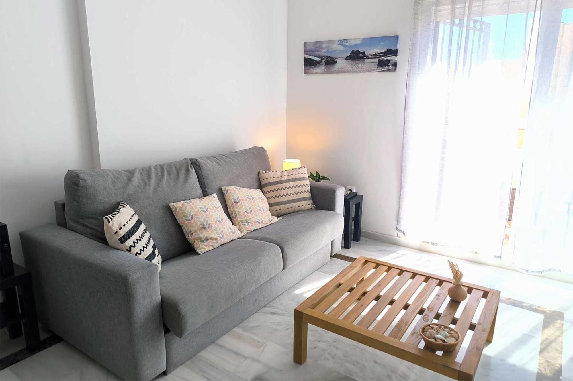 Un salon avec un canapé gris, des coussins à motifs, une table basse en bois et un tableau accroché au mur.