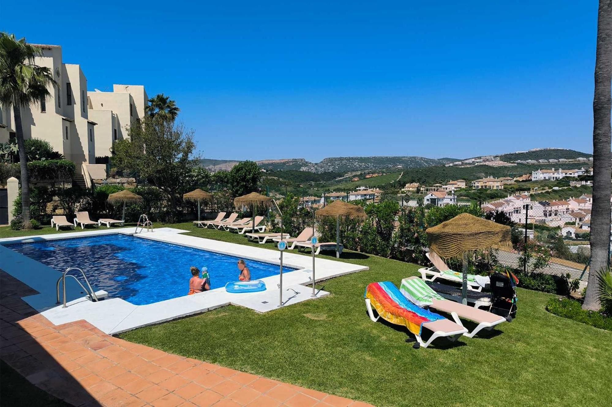 Una piscina con sillas de descanso y sombrillas, rodeada de follaje y con vistas a un paisaje montañoso.