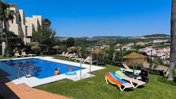Una piscina con sillas de descanso y sombrillas, rodeada de follaje y con vistas a un paisaje montañoso.