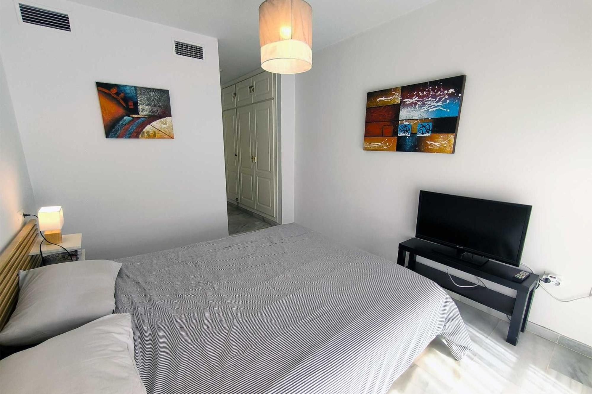 Un dormitorio con cama, televisión y obras de arte en las paredes.