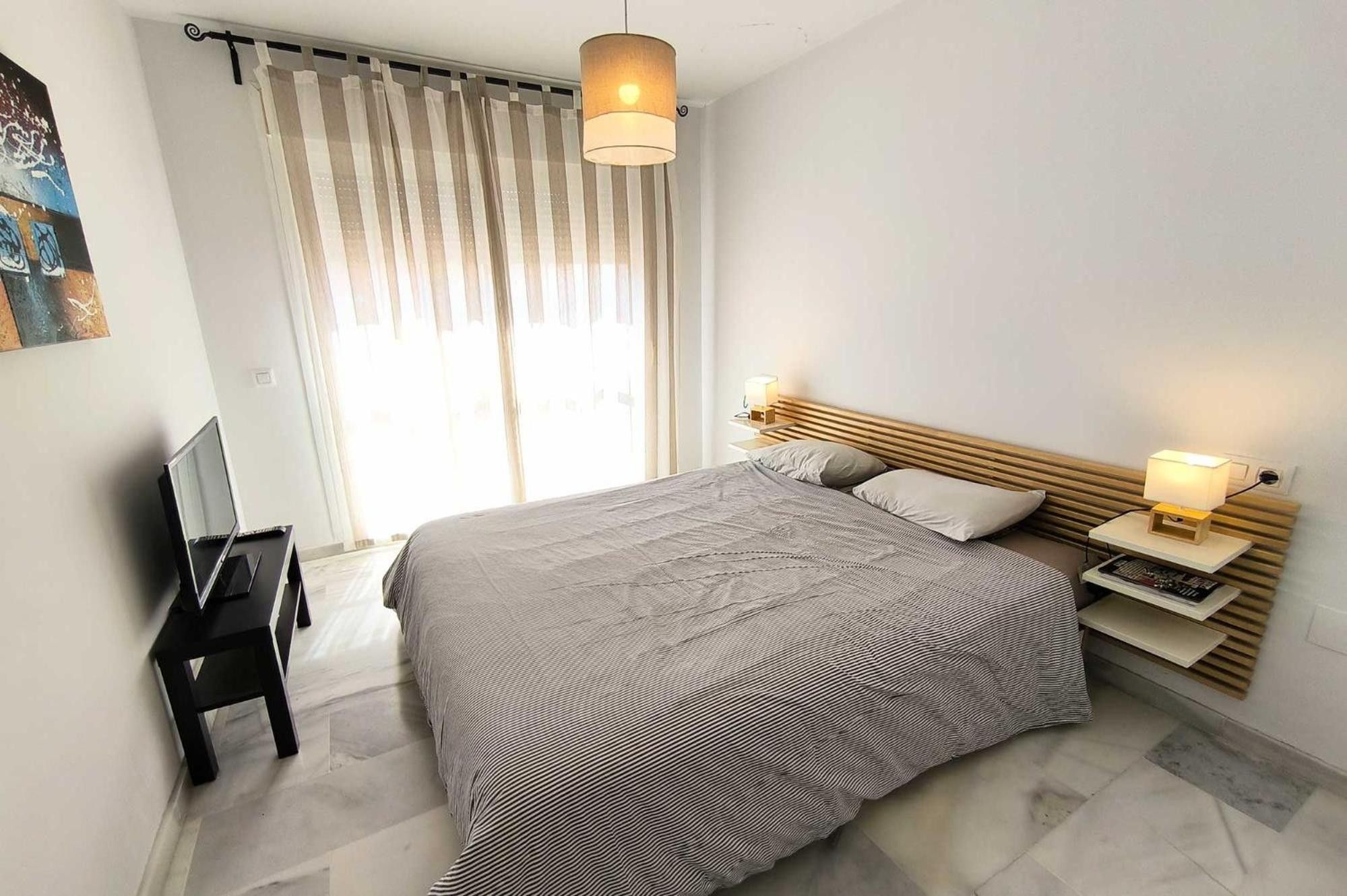 Une chambre moderne avec un grand lit, des lampes de chevet, une télévision et une fenêtre avec des rideaux.