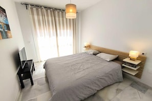 Un dormitorio moderno con una cama grande, lámparas de noche, un televisor y un ventanal con cortinas.