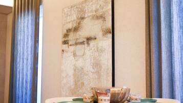 Een eetgedeelte met een tafel voor twee, een groot abstract schilderij aan de muur en blauwe gordijnen.