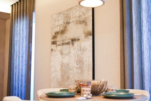 A dining area with a table set for two, a large abstract painting on the wall, and blue curtains. - Vimini Horizon (Bari)