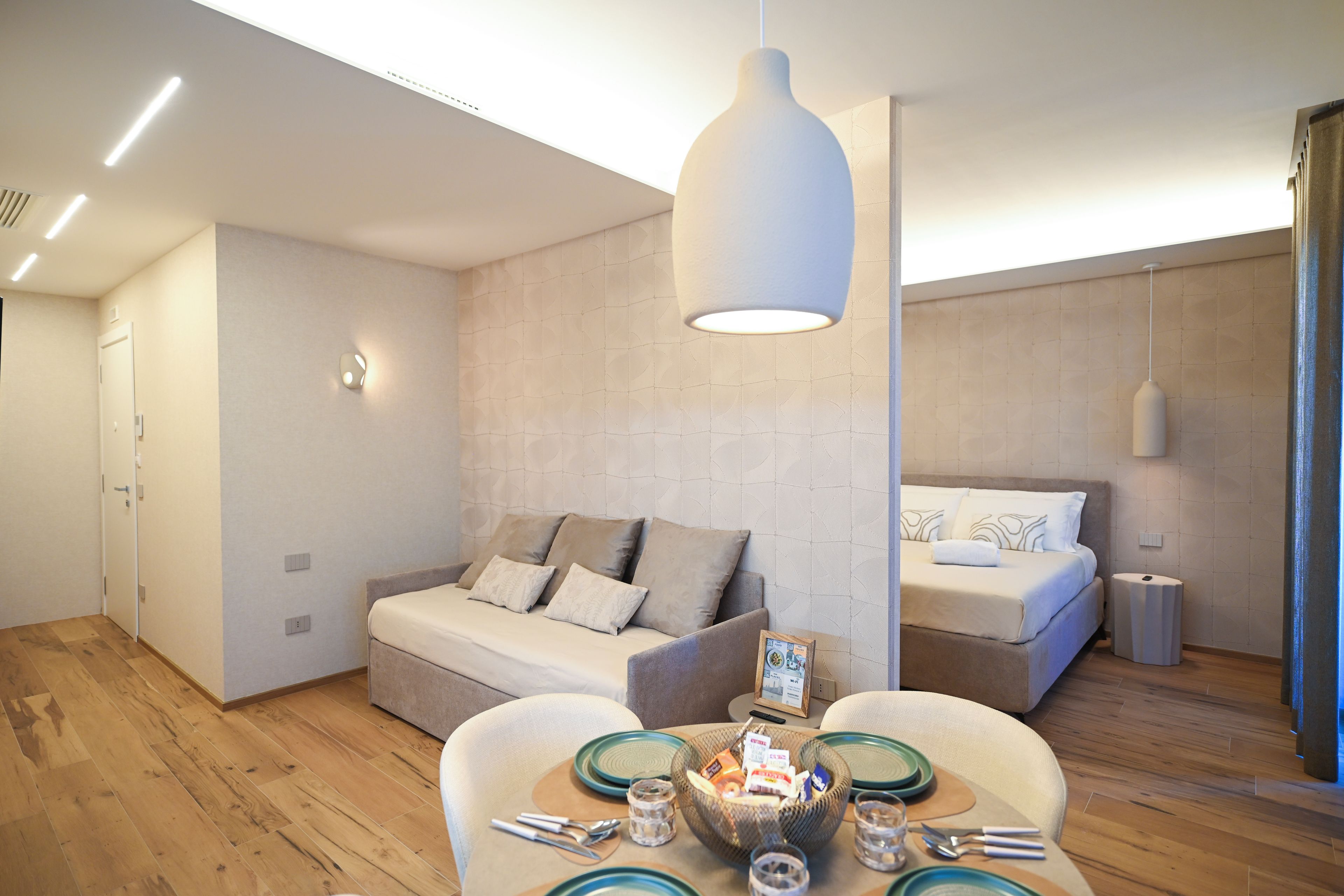 Ein modernes Hotelzimmer mit einer Couch, einem Esstisch mit Tellern und Besteck sowie einem Bett mit Kopfteil.
