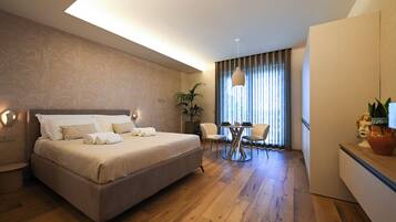 A hotel room with a bed, bedside table, lamp, curtains, and a dining area with chairs and a table.